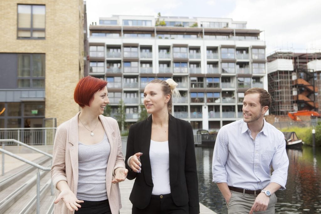Students walking by a canal in East London outside modern student accommodation buildings.