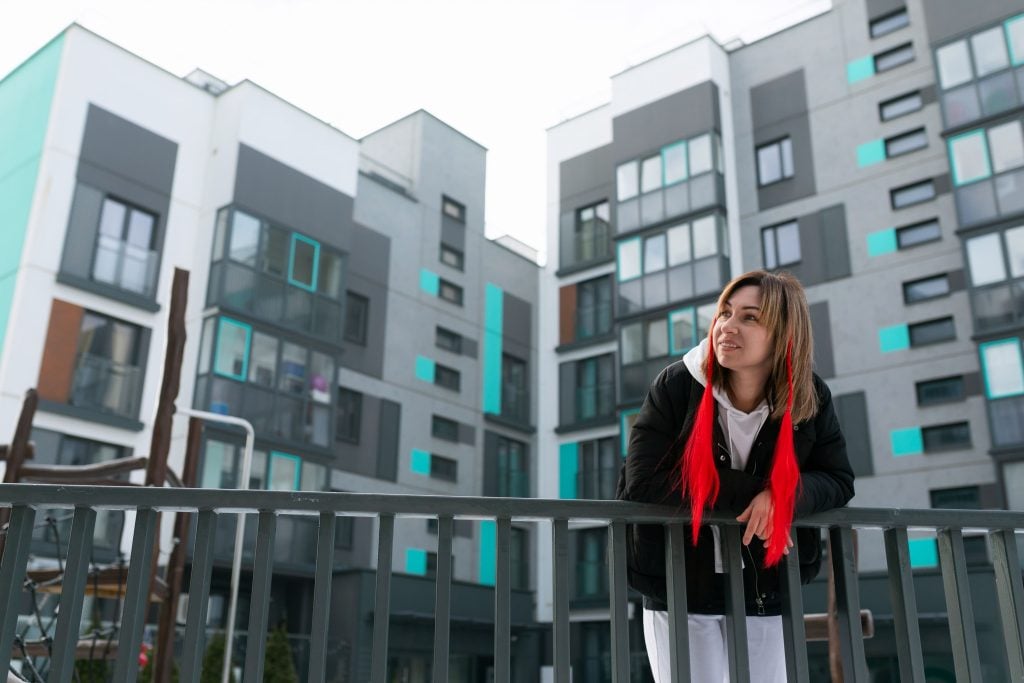 Female student relaxing outside a modern student housing complex with grey and turquoise accents.