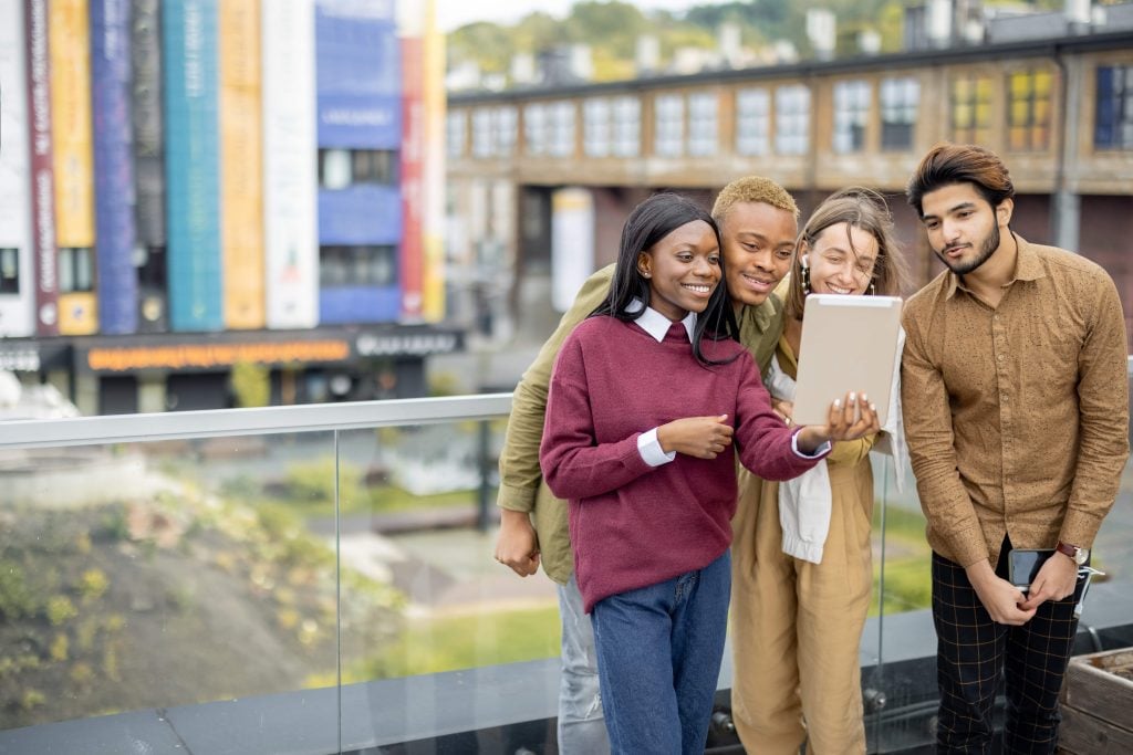 Diverse group of students watching something on a tablet on a student housing balcony.