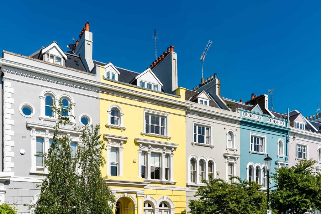 Row of pastel-painted Victorian terraced houses in Notting Hill, London, under a clear blue sky.