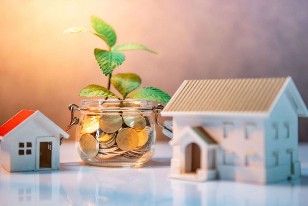 Jar of coins with plant growing beside house models.