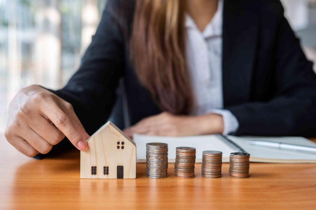 Businesswoman managing property investment finances with a wooden model house and growing stacks of coins, representing strong buy-to-let yields.