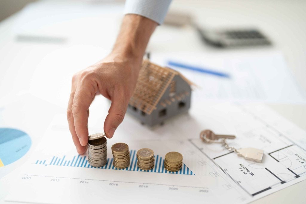 Landlord analysing property investment data, stacking coins on a financial growth chart next to house keys and a property floorplan.