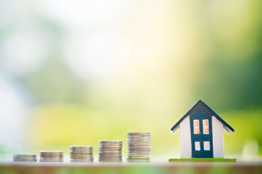 Increasing stacks of coins leading towards a model house against a green background, demonstrating long-term capital growth in the UK private rented sector.