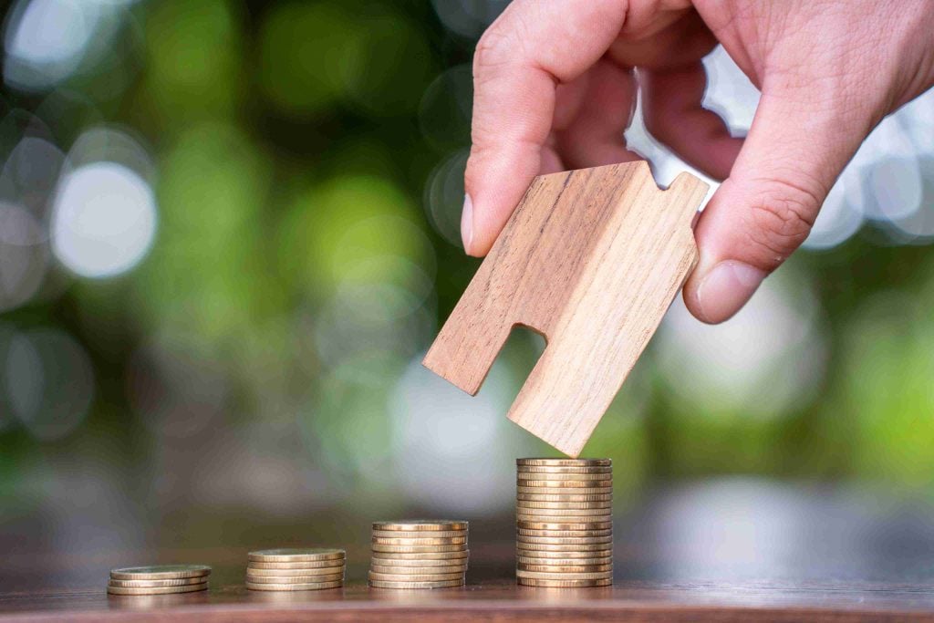 Investor placing a wooden house on top of growing coin stacks, symbolising robust rental yields in purpose-built student accommodation.
