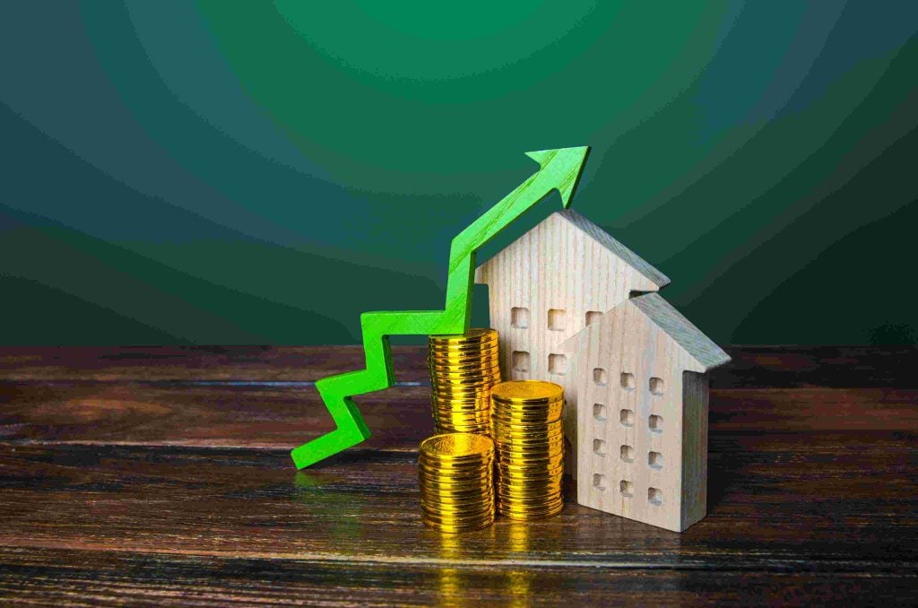 Green upward trending arrow over wooden houses and gold coins, representing the rising market value and profitability of UK property investments.
