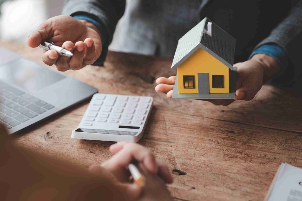 Property consultant discussing off-plan property investment opportunities with a client while holding a yellow model house.