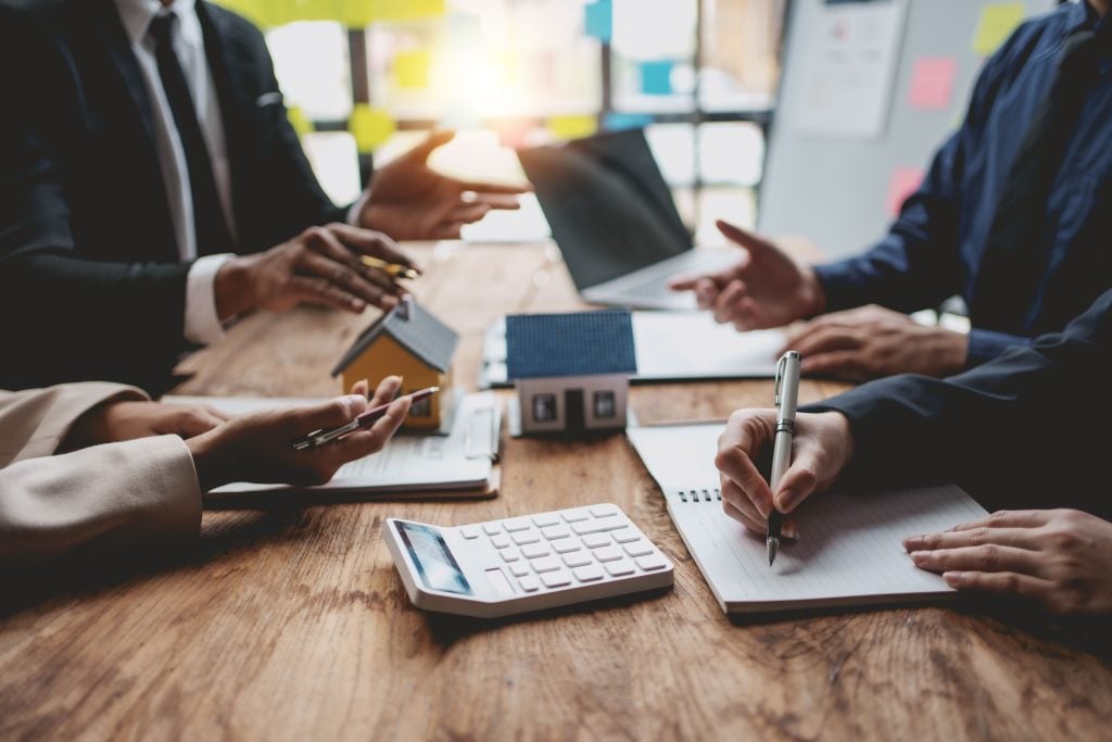 Investors and an adviser reviewing property figures with model houses and a calculator on a desk