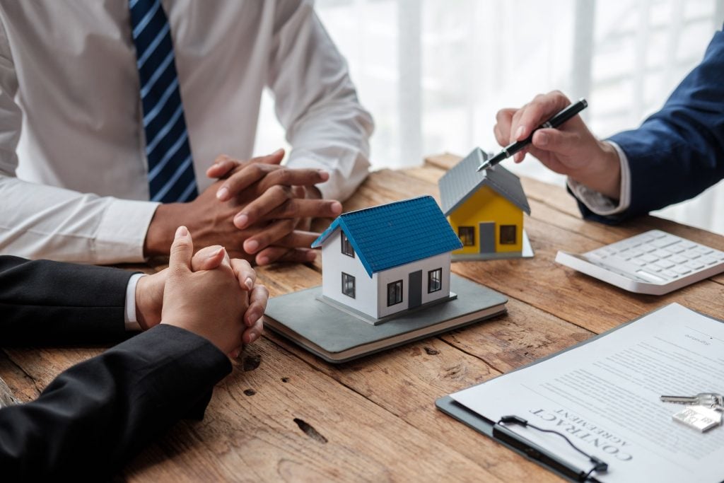 Adviser pointing to two model houses while an investor considers a property contract at a desk