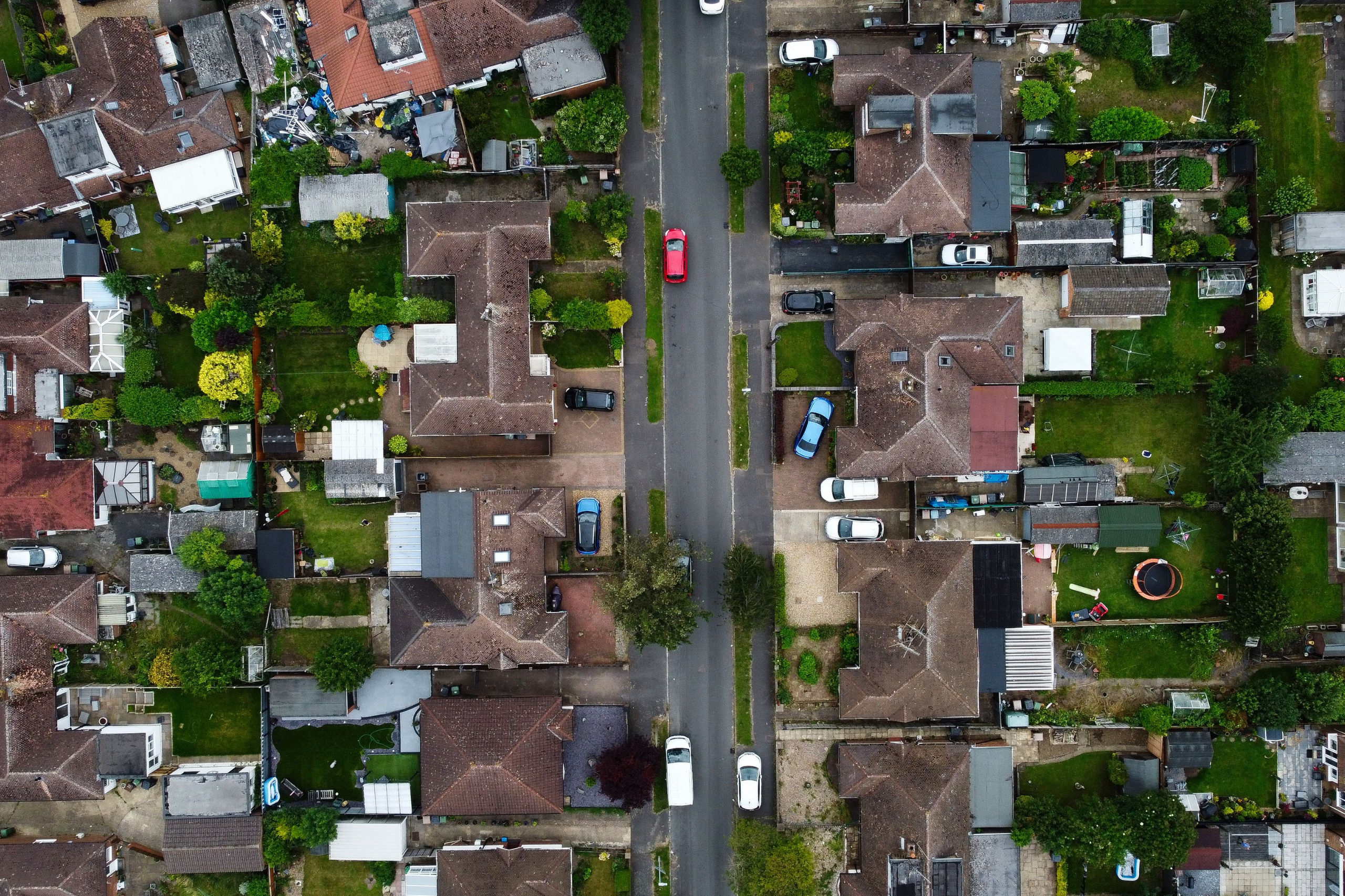 Aerial view of a residential neighbourhood with houses, gardens and parked cars lining a central road.